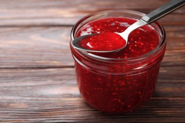 Cam kavanozda tatlı ahududu reçeli ve tahta masada kaşık, yakın plan.