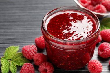 Cam kavanozda tatlı ahududu reçeli ve koyu gri ahşap masada böğürtlen, yakın plan.