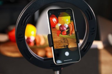 Stüdyoda akıllı telefonla sebze çekmek, ekrana odaklanmak. Profesyonel yemek fotoğrafçılığı.