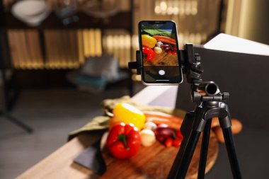 Stüdyoda akıllı telefonla sebze çekmek, ekrana odaklanmak. Profesyonel yemek fotoğrafçılığı.