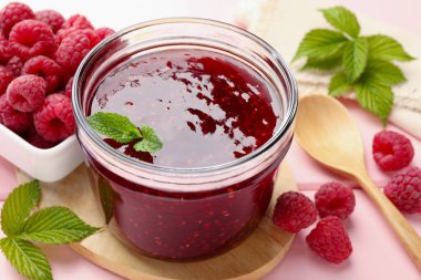 Cam kavanozda tatlı ahududu reçeli, pembe ahşap masada nane ve böğürtlen, yakın plan.