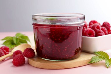 Cam kavanozda tatlı ahududu reçeli, pembe ahşap masada nane ve böğürtlen, yakın plan.