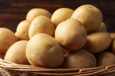 Hasır sepette bir sürü çiğ patates, bulanık kahverengi arka plan, yakın plan.