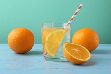 Portakal dilimli maden suyu, taze meyve ve pipetler açık mavi ahşap masa üzerinde turkuaz arka planda