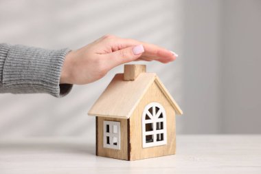 Ev güvenliği. Beyaz masadaki ev modelini koruyan kadın, yakın plan.
