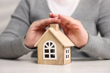 Ev güvenliği. Beyaz masadaki ev modelini koruyan kadın, yakın plan.