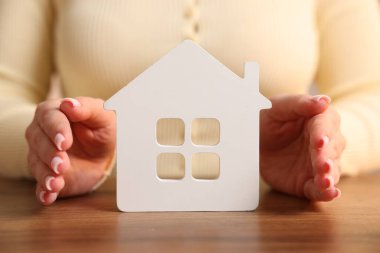 Ev güvenliği. Ahşap masada ev figürlerini koruyan kadın, yakın plan.