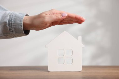 Ev güvenliği. Ahşap masadaki ev figürlerini arka plandaki ışığa karşı koruyan kadın, yakın plan.