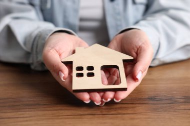 Ev güvenliği. Ahşap masada ev figürlü bir kadın, yakın plan.