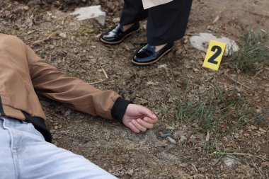 Adli tıp uzmanlığı. Dedektif, olay yerindeki cesedin yanında, dışarıda, yakın mesafede.