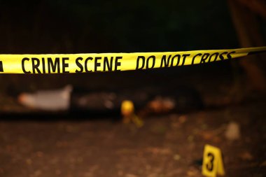 Adli tıp uzmanlığı. Cesedin bulunduğu suç mahalli, kanıt, işaretleyiciler ve polis bandı açık havada, seçici odaklanma