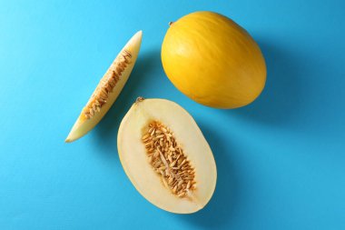 Açık mavi arka planda olgun kavunların tamamı ve kesimi düzdü.