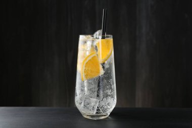 Portakal dilimli soda ve siyah ahşap masada buzlu cam.