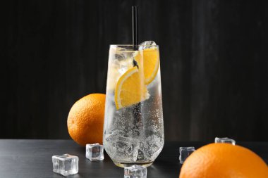 Portakal dilimleri ve siyah ahşap masa üzerindeki buz küpleriyle soda tazeleniyor.