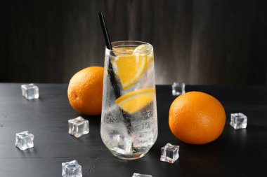 Portakal dilimleri ve siyah ahşap masadaki buz küpleriyle soda tazeleniyor.