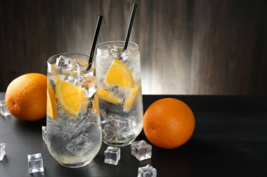 Portakal dilimleri ve siyah ahşap masadaki buz küpleriyle soda tazeleniyor. Yakın plan. Metin için boşluk