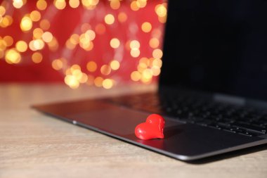 Online flört sitesi. Kırmızı kalp ve laptop ahşap masada bulanık ışıklara karşı, yakın plan. Bokeh etkisi