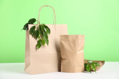 Farklı çevre dostu ambalajlar ve açık yeşil arka plana karşı beyaz masada bırakmalar