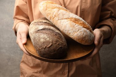 Gri arka planda taze ekmek somunları olan kadın, yakın plan.