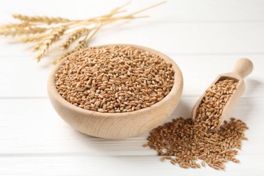 Kasede buğday taneleri, beyaz ahşap masada kepçe ve çiviler, yakın plan.