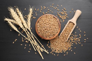 Kâsede buğday taneleri, siyah ahşap masada kepçeler ve çiviler, düz uzanmış.