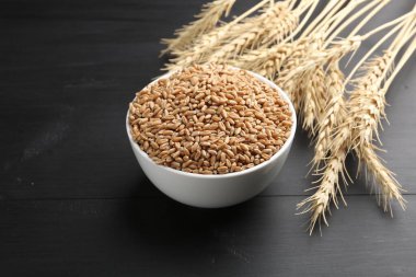 Kasede buğday taneleri ve siyah ahşap masada çiviler, yakın plan. Metin için boşluk