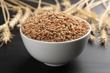 Kasede buğday taneleri ve siyah ahşap masada çiviler, yakın plan.