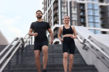 Spor giyimli kadın ve erkek merdivenlerden aşağı koşuyor, hareket mavisi etkisi. Düşük açı görünümü