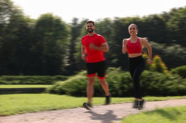 Güneşli bir sabahta spor giyinen erkek ve kadın açık havada koşuyor, hareket mavisi etkisi.