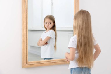 Küçük kız aynanın içinde üzgün yansımasına bakıyor. Ruh Sağlığı