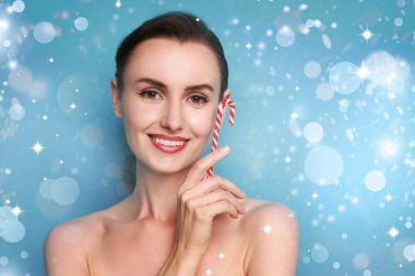 Gülümseyen kadın mükemmel makyajlı açık mavi arka planda Noel şekeri kamışı tutuyor.