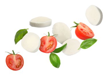 Mozzarella peyniri, domates ve fesleğen yaprakları beyaz arka planda uçuşuyor.