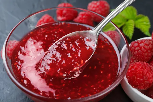 Gri masadaki cam kaseden kaşıkla ahududu reçeli alıp...