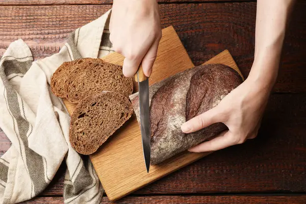 Ahşap masada taze ekmek kesen bir kadın.