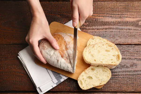 Ahşap masada taze ekmek kesen bir kadın.