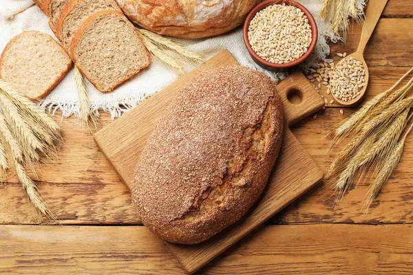Farklı türde ekmek, tahıl ve buğday çivileri ahşap masada, düz yerde.
