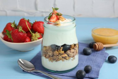 Tahıllı yoğurt, böğürtlen, bal ve kaşık açık mavi ahşap masa, yakın plan.