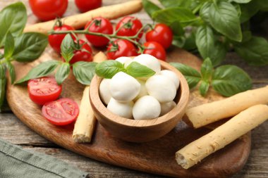 Lezzetli mozzarella peyniri topları, domatesler, fesleğen ve grissini ahşap masada, yakın plan.