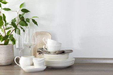 Mutfaktaki tezgahta farklı beyaz bulaşık takımları, bardaklar ve bitkiler var.