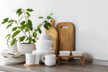 Farklı beyaz bulaşık takımları, ahşap kesim tahtaları, çatal bıçak takımı ve mutfak tezgahı.