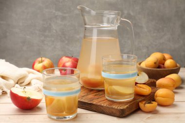 Bardaklar, sürahiler, taze kayısılar ve ahşap masada elmalar.