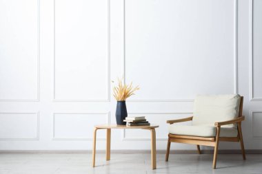 Konforlu bej koltuk, vazo ve kitaplarla dolu masa. Beyaz duvarın yanında, yazı için yer.