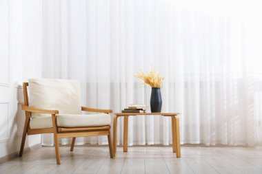 Konforlu bej koltuk, vazo ve kitaplarla dolu masa.