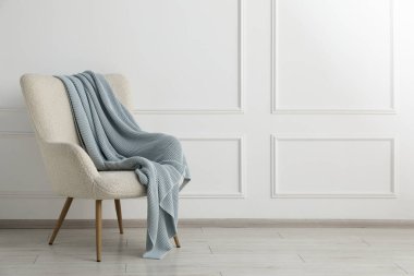 Beyaz duvarın yanında battaniyesi olan rahat koltuk, metin için boşluk.