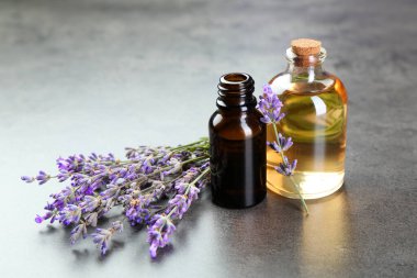 Şişelerdeki yağlar ve gri desenli masadaki lavanta çiçekleri, yakın plan.