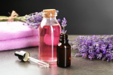 Şişelerdeki yağlar, damlacıklar ve lavanta çiçekleri gri desenli masa ve koyu arkaplan, yakın plan