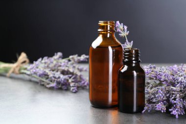 Şişelerdeki Aromatik yağlar ve gri desenli masadaki lavanta çiçekleri koyu arka planda, yakın plan. Metin için boşluk