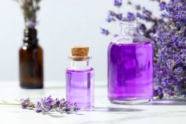 Şişelerdeki Aromatik yağ ve beyaz mermer masadaki lavanta çiçekleri açık gri arka planda, yakın plan