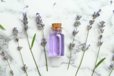 Beyaz mermer sehpanın üzerinde lavanta çiçekleri ve şişede yassı yağ var.