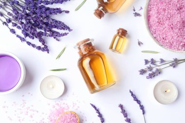 Şişelerde aromatik esanslı yağ, lavanta çiçekleri ve beyaz masada deniz tuzu içeren spa kompozisyonu.